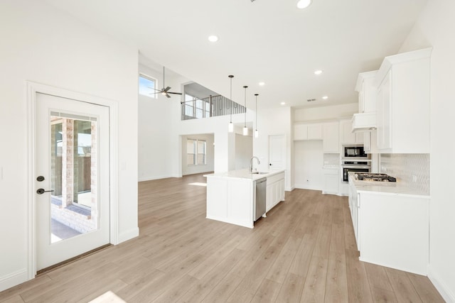 kitchen with a sink, open floor plan, stainless steel appliances, light wood-style floors, and light countertops