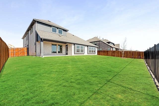 rear view of house with a yard, brick siding, roof with shingles, and a fenced backyard