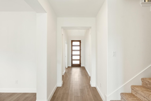 hallway featuring stairway, baseboards, and light wood-style floors