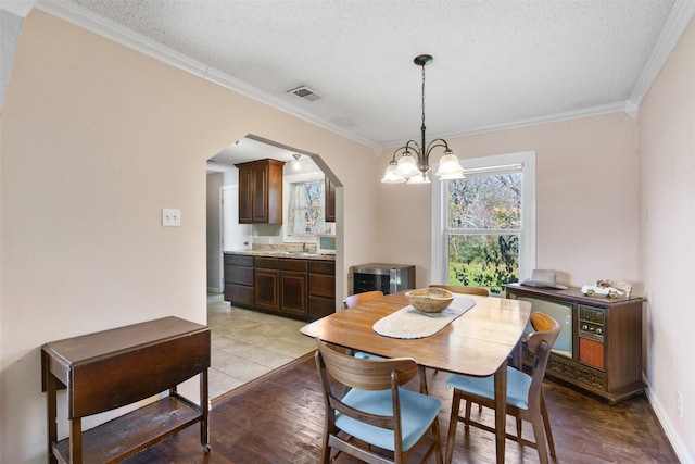 dining area with sink, crown molding, a chandelier, light hardwood / wood-style flooring, and a textured ceiling