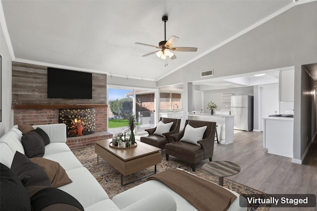 living room with sink, crown molding, ceiling fan, a fireplace, and light hardwood / wood-style floors