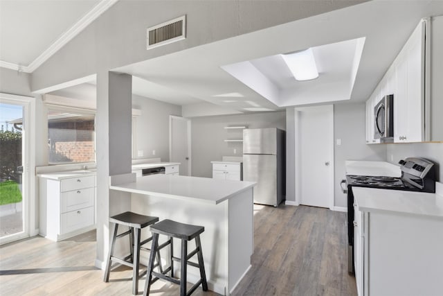 kitchen with a kitchen breakfast bar, crown molding, hardwood / wood-style floors, white cabinets, and appliances with stainless steel finishes