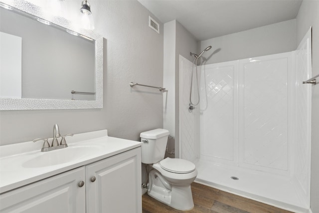 bathroom featuring wood-type flooring, walk in shower, vanity, and toilet