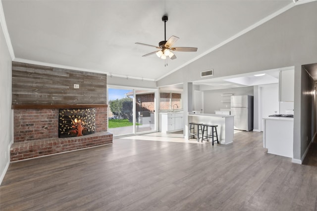 unfurnished living room featuring a brick fireplace, crown molding, wood-type flooring, and ceiling fan