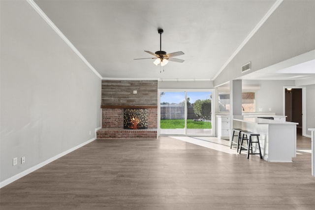 unfurnished living room with ceiling fan, crown molding, hardwood / wood-style floors, vaulted ceiling, and a fireplace