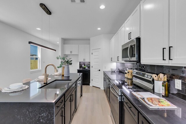 kitchen featuring ceiling fan, hanging light fixtures, stainless steel appliances, white cabinets, and a center island with sink