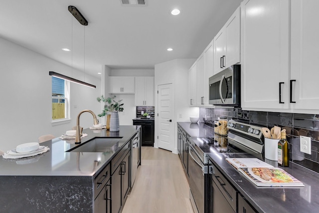 kitchen featuring dark countertops, light wood-style flooring, appliances with stainless steel finishes, and a sink