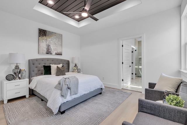 bedroom with ceiling fan, ensuite bathroom, a raised ceiling, and light hardwood / wood-style flooring