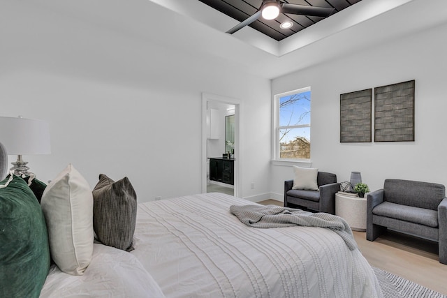 bedroom featuring a raised ceiling, ensuite bath, ceiling fan, and light hardwood / wood-style flooring