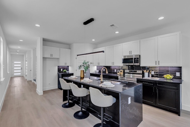 kitchen with decorative light fixtures, a center island with sink, dark countertops, appliances with stainless steel finishes, and a sink