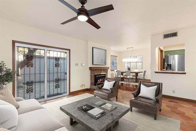 living room featuring ceiling fan, a fireplace, and tile patterned flooring