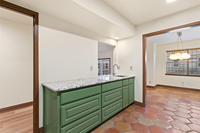 kitchen with hanging light fixtures, light stone counters, green cabinetry, and sink