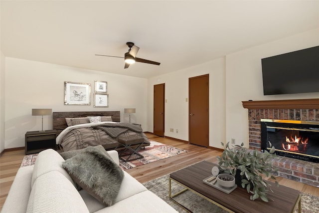 bedroom featuring a brick fireplace, ceiling fan, and light hardwood / wood-style flooring