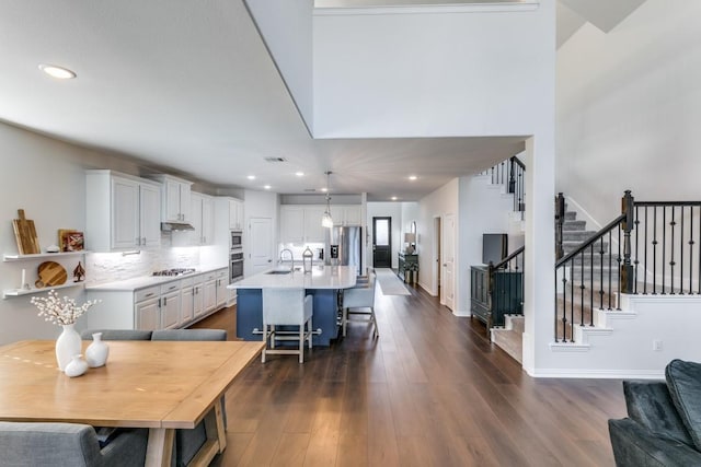 kitchen with stainless steel appliances, a center island with sink, white cabinetry, and dark hardwood / wood-style floors