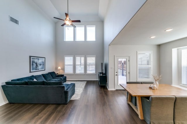 living room with ceiling fan, dark wood-type flooring, plenty of natural light, and a high ceiling