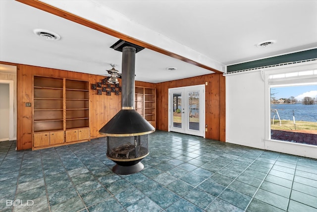 unfurnished living room with a water view, built in shelves, a wood stove, and wood walls