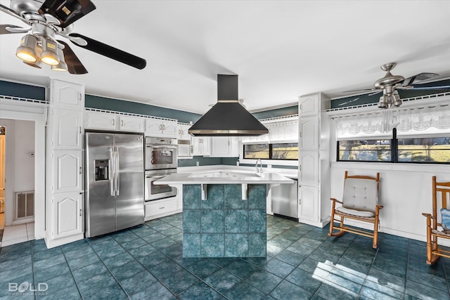 kitchen with ceiling fan, a center island, stainless steel appliances, island range hood, and white cabinets