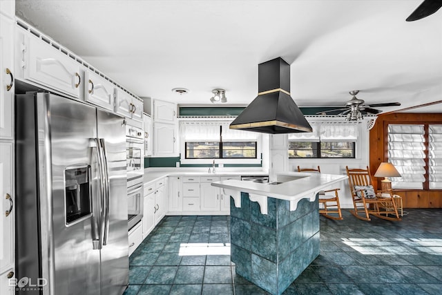 kitchen featuring a breakfast bar, white cabinetry, island range hood, appliances with stainless steel finishes, and ceiling fan