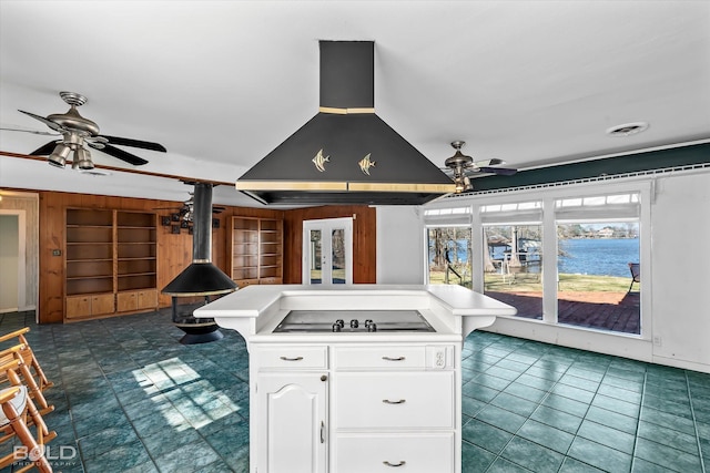 kitchen featuring a wood stove, a kitchen island, stovetop, island range hood, and white cabinets