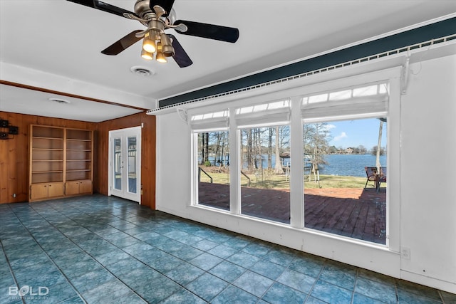 unfurnished room featuring french doors, built in shelves, ceiling fan, a water view, and wood walls