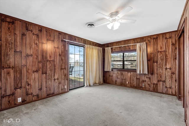 carpeted empty room with ceiling fan, a water view, and wooden walls