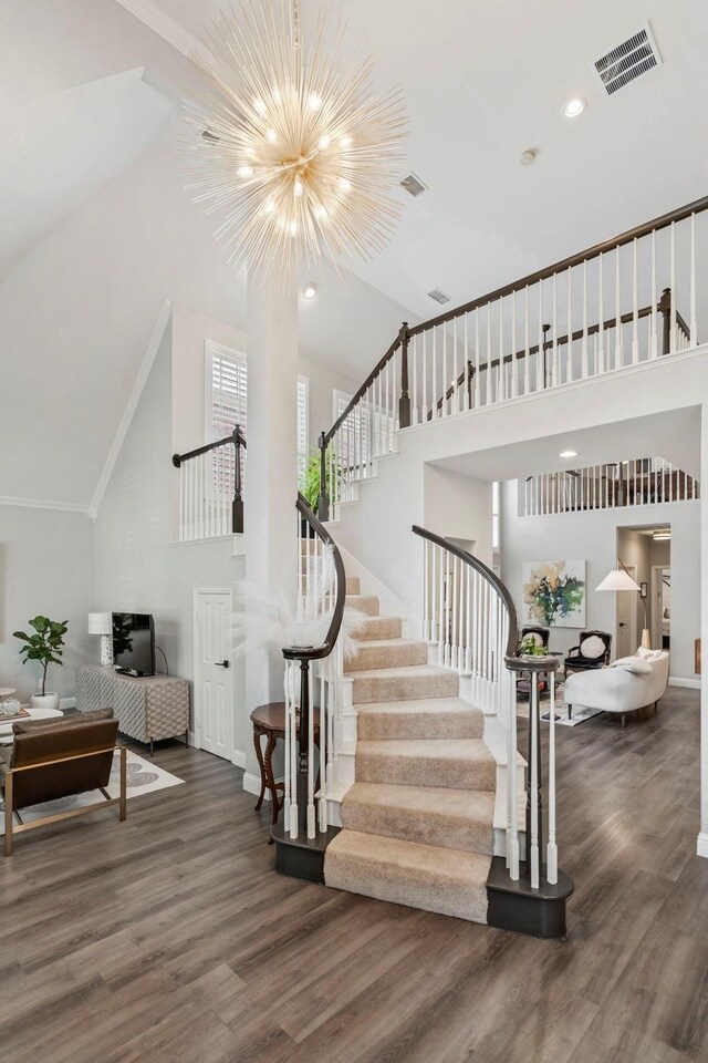 stairs featuring crown molding, high vaulted ceiling, a chandelier, and wood-type flooring