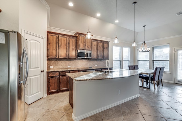 kitchen with an island with sink, pendant lighting, stainless steel appliances, light stone countertops, and backsplash