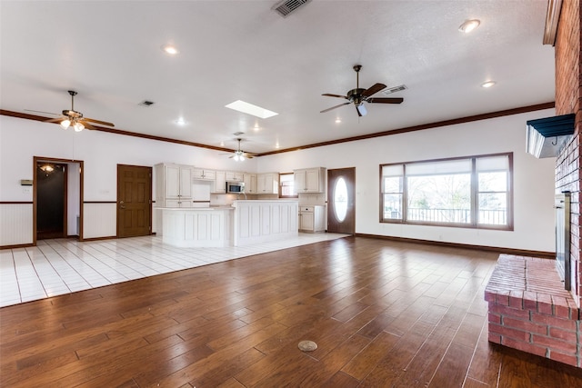 unfurnished living room with a skylight, crown molding, and light hardwood / wood-style flooring