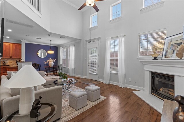 living room featuring ceiling fan, dark hardwood / wood-style flooring, a high ceiling, and ornamental molding