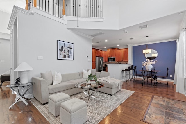 living room featuring a towering ceiling, dark wood-type flooring, and crown molding