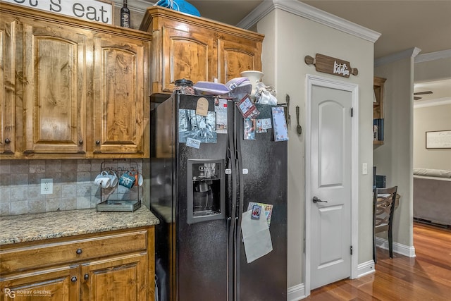 kitchen with light stone countertops, backsplash, ornamental molding, black fridge with ice dispenser, and wood-type flooring