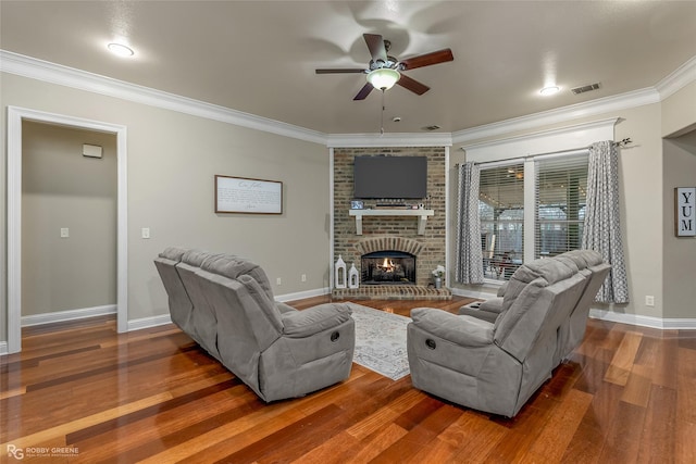 living room with dark wood-type flooring, a brick fireplace, ceiling fan, and crown molding