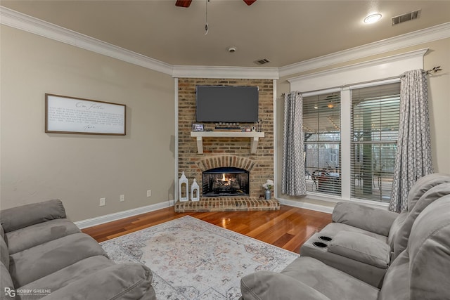 living room with ceiling fan, wood-type flooring, ornamental molding, and a brick fireplace