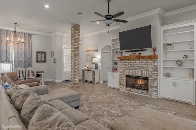 living room featuring light wood-type flooring, ceiling fan with notable chandelier, a brick fireplace, and a healthy amount of sunlight