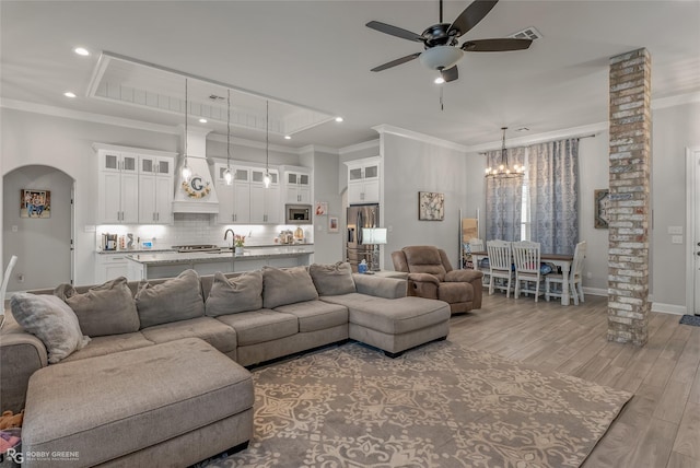 living room featuring sink, a raised ceiling, light wood-type flooring, ceiling fan with notable chandelier, and ornamental molding