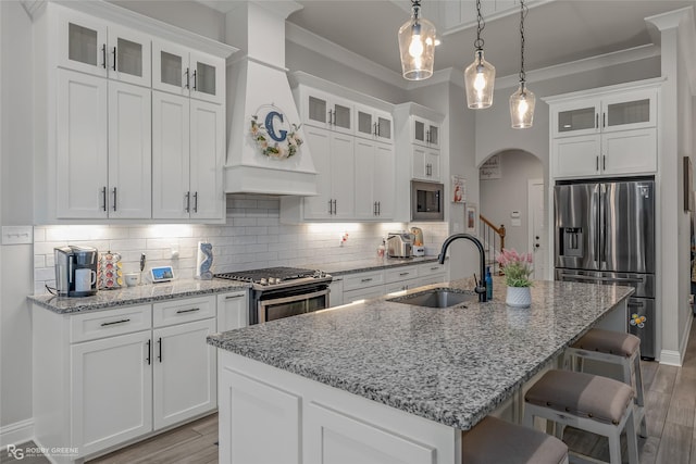 kitchen featuring light stone counters, an island with sink, decorative light fixtures, white cabinets, and appliances with stainless steel finishes