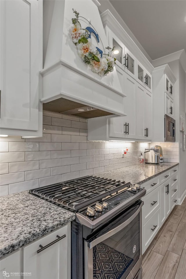 kitchen with white cabinets, custom range hood, light stone counters, and stainless steel gas range oven