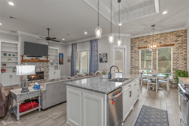 kitchen featuring white cabinets, a center island with sink, sink, a brick fireplace, and stainless steel appliances