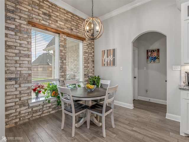 dining space featuring light hardwood / wood-style floors, crown molding, brick wall, and an inviting chandelier