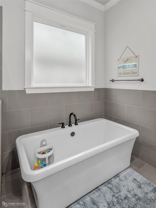 bathroom with ornamental molding, tile patterned floors, tile walls, and a bathing tub