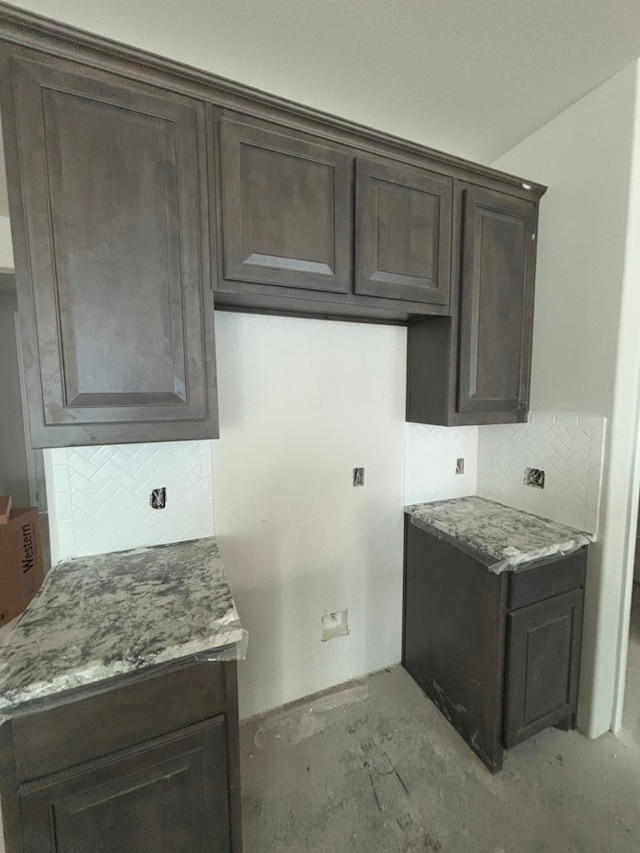 kitchen featuring decorative backsplash, light stone countertops, and dark brown cabinets