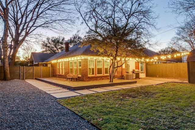 back house at dusk featuring a lawn and a patio area