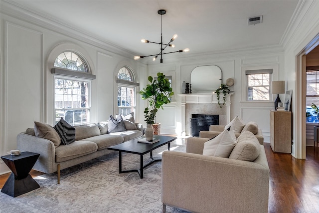 living room with hardwood / wood-style floors, ornamental molding, a notable chandelier, and a premium fireplace