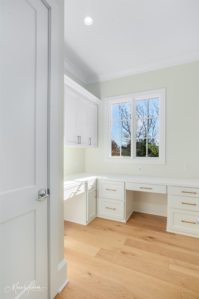 unfurnished office featuring crown molding, built in desk, and light wood-type flooring