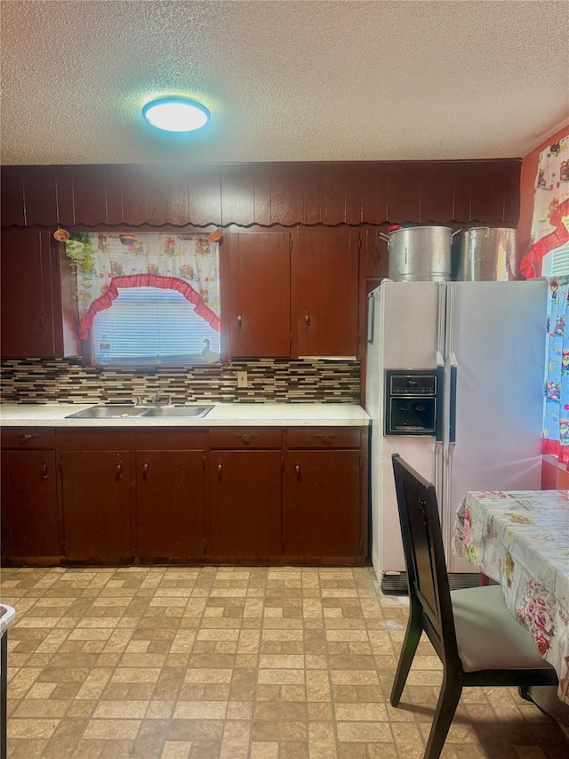 kitchen featuring white refrigerator with ice dispenser, backsplash, sink, and a textured ceiling