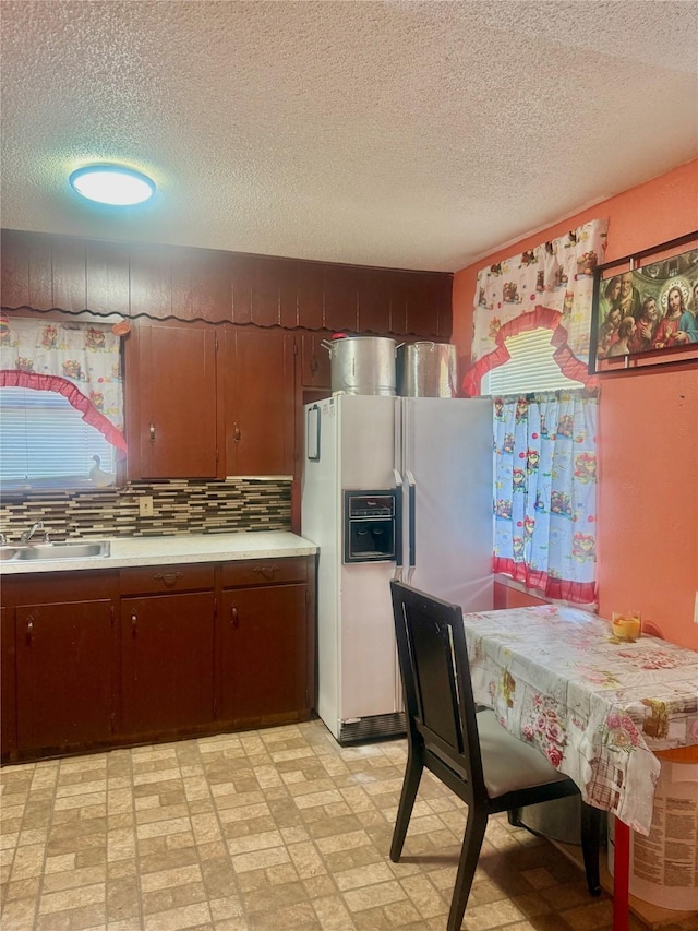 kitchen featuring sink, white fridge with ice dispenser, a textured ceiling, and backsplash