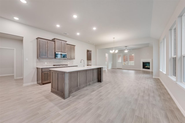 kitchen featuring light countertops, stainless steel microwave, decorative backsplash, open floor plan, and a sink