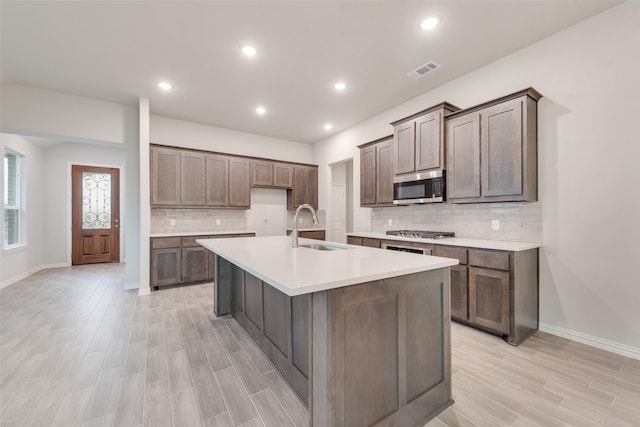 kitchen with stainless steel appliances, a sink, visible vents, wood tiled floor, and a center island with sink