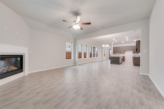 unfurnished living room featuring visible vents, light wood-style flooring, a glass covered fireplace, baseboards, and ceiling fan with notable chandelier