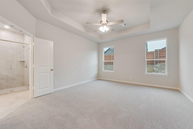 carpeted empty room featuring a ceiling fan, a raised ceiling, visible vents, and baseboards